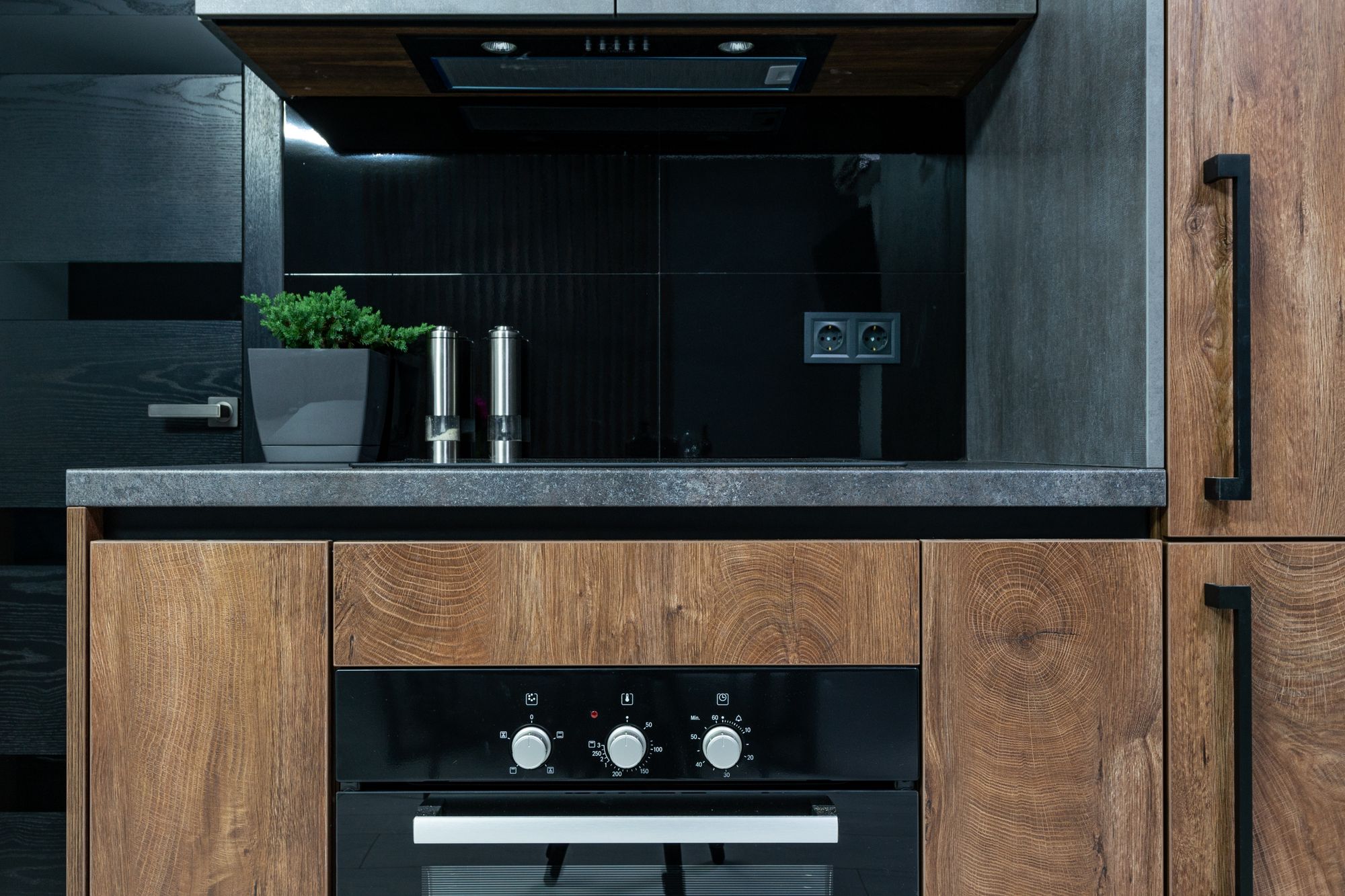 A dark oak and black kitchen with an integrated oven and stone counter