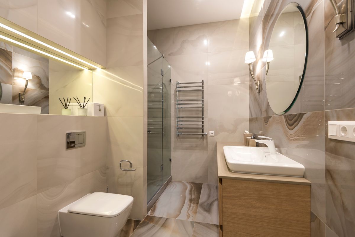 A bathroom in white marble tile with a large mirror and brushed fixtures